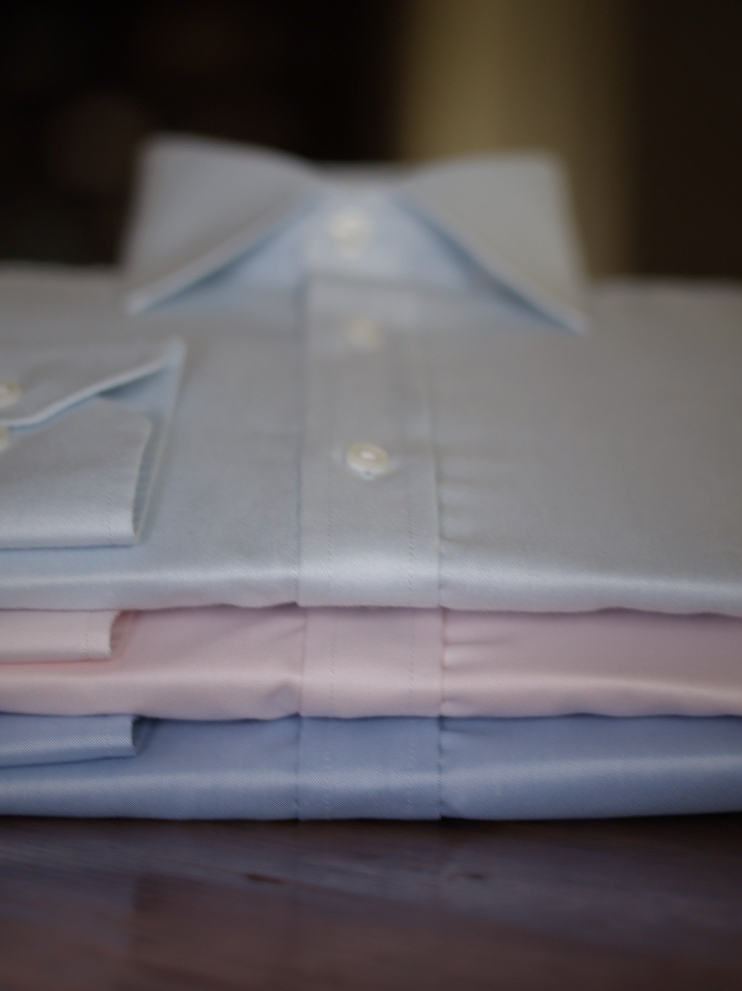 Camisas formales blanca, rosada y azul cielo apiladas sobre una mesa de madera